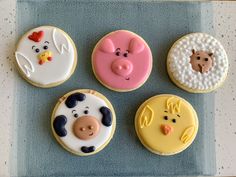 four decorated cookies in the shape of farm animals and pigs on a blue tray with white speckles