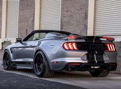 the rear end of a silver sports car parked in front of a building with shutters