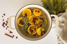 a pot filled with oranges and spices on top of a white table next to some herbs