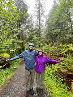 a man and woman standing on a path in the woods with their arms spread out