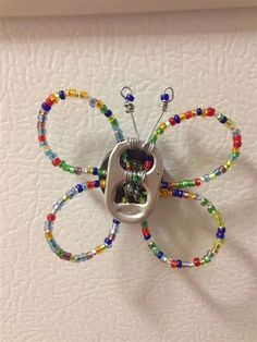 a metal butterfly with colorful beads on it's wings hanging from a white wall