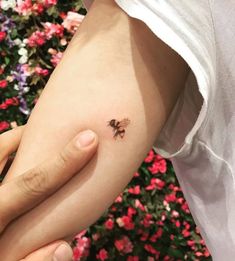 a person holding their arm with a small tattoo on it's left side, in front of flowers