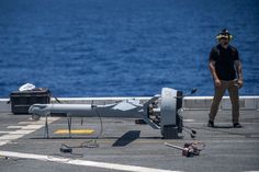 a man standing on the deck of an aircraft carrier with equipment scattered around it and in front of him