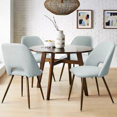 a dining room table with four chairs and a vase on the top of it in front of a white brick wall