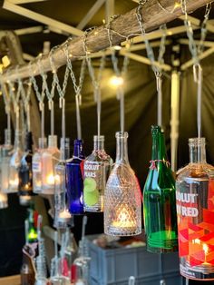 many different colored glass bottles hanging from a wooden beam with string lights attached to them