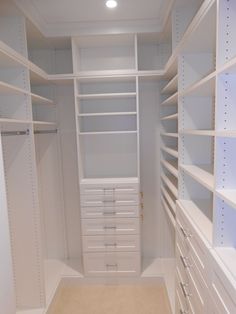 an empty walk in closet with white shelves and drawers