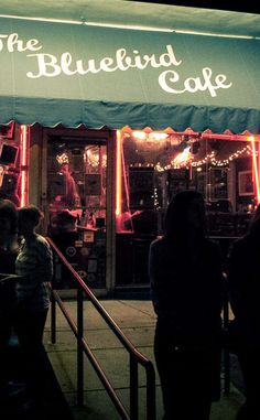 the bluebird cafe is lit up at night with people standing outside and looking in