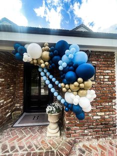 blue and gold balloons are hanging from the side of a brick building in front of a potted plant