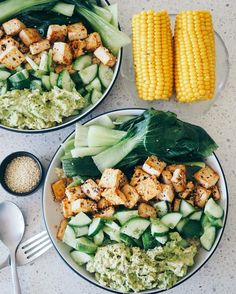 two plates filled with food next to corn on the cob and broccoli