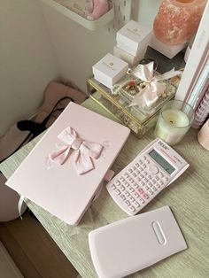 a pink box with a bow on it next to a calculator and candle