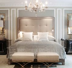 a bedroom with a large bed, chandelier and two mirrors on the wall