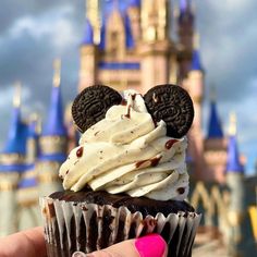 a cupcake with white frosting and mickey mouse ears on top in front of a castle