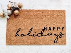 a welcome mat with the words happy holidays written in black on it and ornaments around it