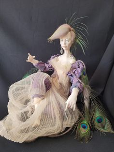 a doll sitting on top of a black surface with a peacock tail in it's hand