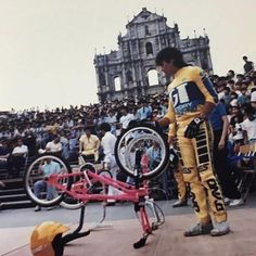 a man standing next to a red bike on top of a stage in front of a crowd