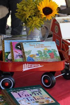 a red wagon filled with books sitting on top of a table next to a sunflower