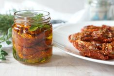 a jar filled with pickled tomatoes next to a plate full of dried tomatoes and herbs