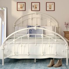 a white bed sitting in a bedroom next to a wooden dresser and table with two framed pictures on the wall