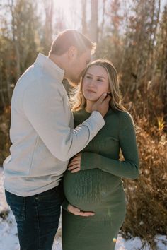 a pregnant couple cuddles in the snow while holding each other's belly