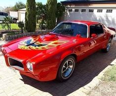 a red car with flames painted on the hood parked in front of a garage door