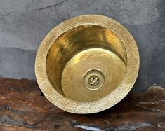 a gold sink sitting on top of a wooden table next to a gray stone wall