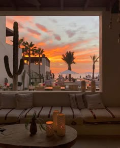 the sun is setting over an outdoor lounge area with cactus in the foreground and palm trees on the other side