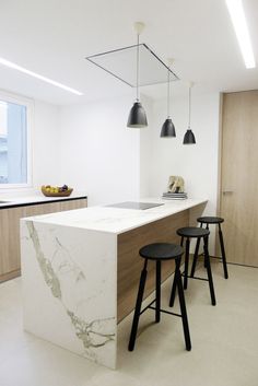 a kitchen with marble counter tops and stools in front of the island, along with two black pendant lights