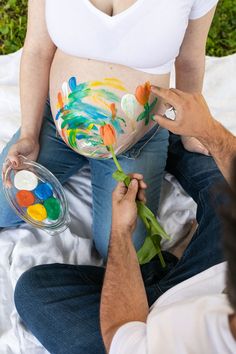 a pregnant woman sitting on top of a bed next to a man holding a flower