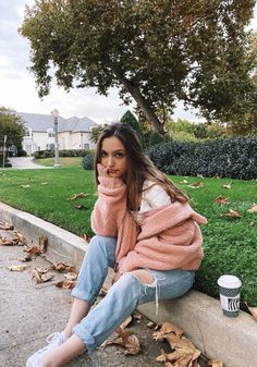 a woman sitting on the curb with her hand in her mouth and looking at the camera