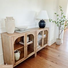 a wooden cabinet sitting on top of a hard wood floor next to a white vase