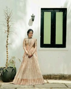 a woman standing in front of a white building wearing a pink lehenga and matching jewelry