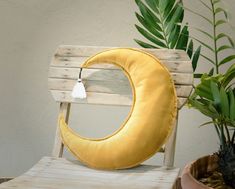 a yellow crescent pillow sitting on top of a wooden bench next to a potted plant