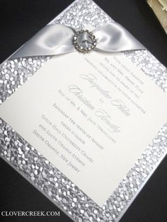 the wedding card is decorated with silver sequins and a bow on it's side