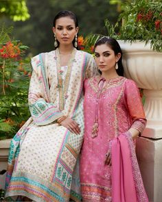 two women standing next to each other in front of flowers and plants, wearing colorful clothing