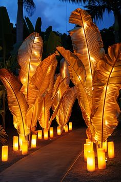 many lit candles are lined up along a path with palm leaves on the sides and in front of them