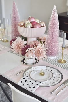 a table set for christmas with pink decorations and white plates, silver utensils