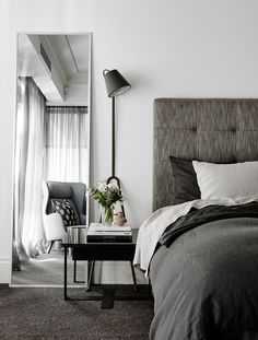 a bedroom with a bed, nightstand and chair in it's corner area next to a large mirror