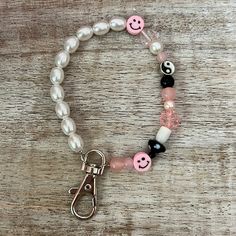 a beaded bracelet with pink, black and white beads has a smiley face charm on it