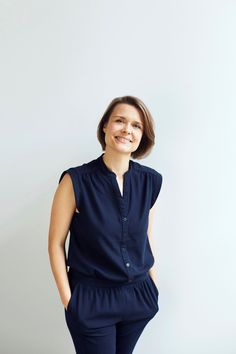 a woman standing in front of a white wall with her hands on her hips and smiling