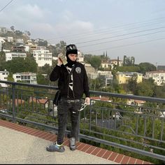 a man standing on top of a balcony next to a metal railing with buildings in the background