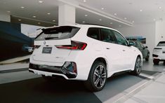 the rear end of a white bmw suv parked in a showroom with other cars