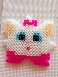 a cat made out of legos sitting on top of a white surface with pink, yellow and blue beads