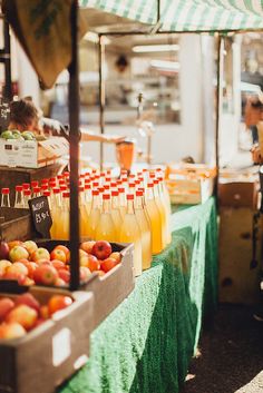 an outdoor fruit stand with orange juice and apples