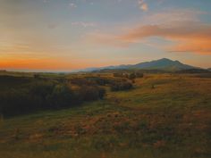 the sun is setting over an open field with mountains in the distance