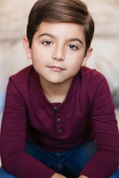 a young boy is sitting on the floor with his hands crossed and looking at the camera