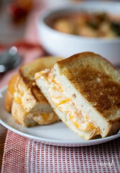 two grilled cheese sandwiches on a plate with a bowl of soup in the background