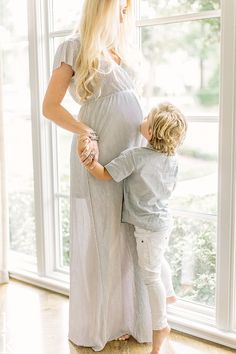 a pregnant woman holding her son's hand while standing in front of a window