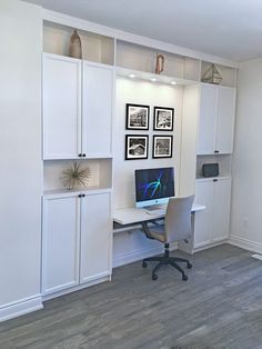 a desk with a computer on top of it in front of some white cupboards