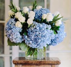 a vase filled with blue and white flowers on top of a wooden table next to a window