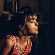 a woman with long hair and green eyeshadow sitting in a dark room looking off into the distance